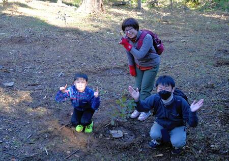 植樹した木と一緒にカメラ目線でポーズをとっている家族の様子