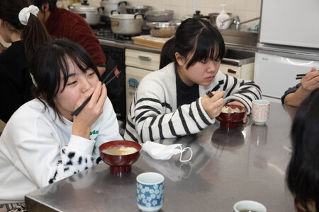 調理台の前に座って、グループで豚汁を食べている様子