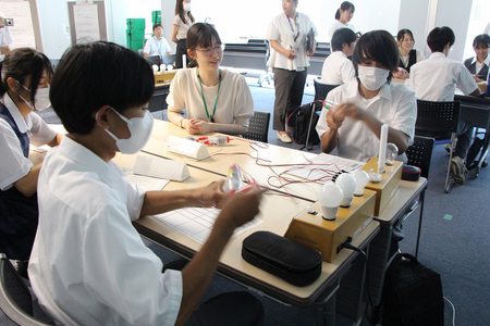 何人が手回し発電機を使って、発電すれば白熱灯が点灯するか実験している様子