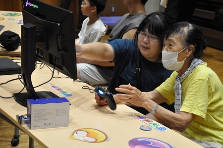 女性が年配の女性に操作を教えながらプレイしている。